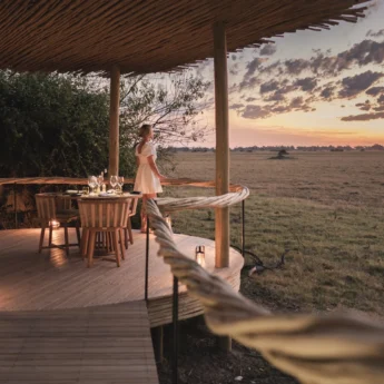 Woman stands on wooden decking watching sunset, Mombo, Moremi Game Reserve, Botswana - Yellow Zebra Safari