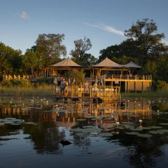 A waterside view of a floating decking and the main lodge which overlooks the water, DumaTau, Botswana - Yellow Zebra Safaris