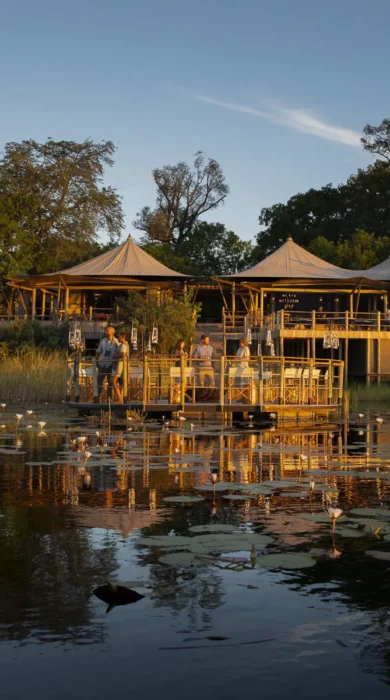 A waterside view of a floating decking and the main lodge which overlooks the water, DumaTau, Botswana - Yellow Zebra Safaris