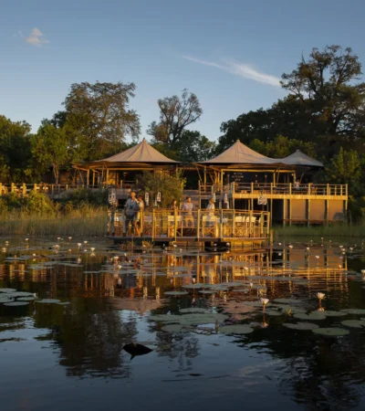 A waterside view of a floating decking and the main lodge which overlooks the water, DumaTau, Botswana - Yellow Zebra Safaris