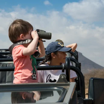 A young boy looks through binoculars whilst standing on a safari truck, Marataba Safari Lodge, Marakele, South Africa - Yellow Zebra Safari