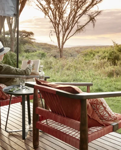 A woman sketches on wooden decking overlooking the reserve, Tanzania - Yellow Zebra Safari