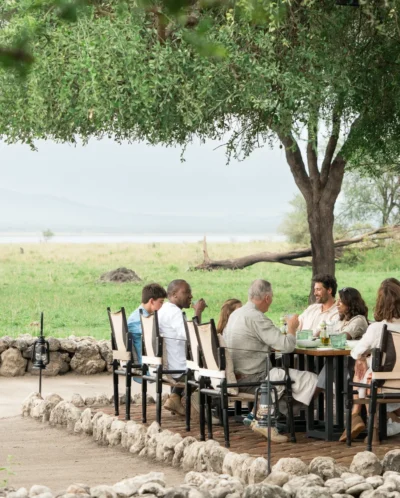 A large group dines around a table beneath an overhanging tree, Little Chem Chem, Tarangire national park, Tanzania - Yellow Zebra Safari