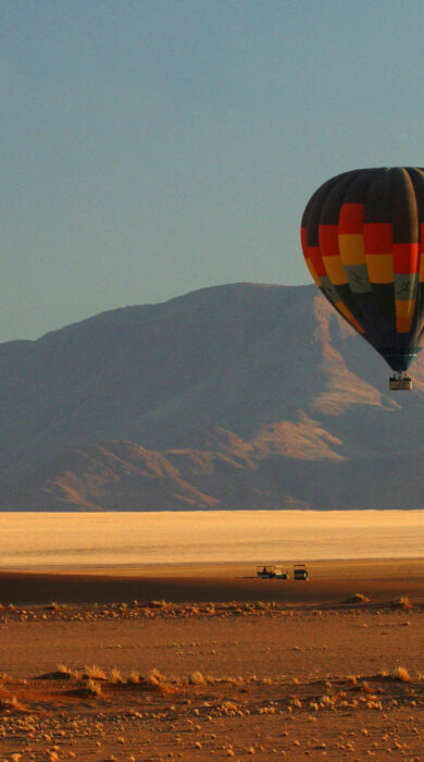 Hot air balloon rises over red dust plains, Wolwedans Plains Camp, Namibia - Yellow Zebra Safaris