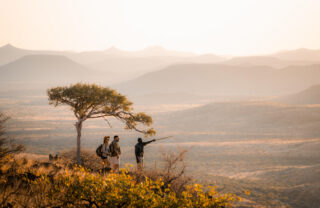 Guests and hide stop under acacia tree on a hike, Damaraland, Namibia - Yellow Zebra Safaris