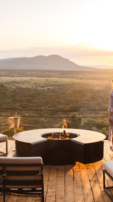 A woman stands on a raised wooden deck overlooking the Mara, Cottars Bush Villa, Greater Mara Conservancy, Kenya - Yellow Zebra Safari