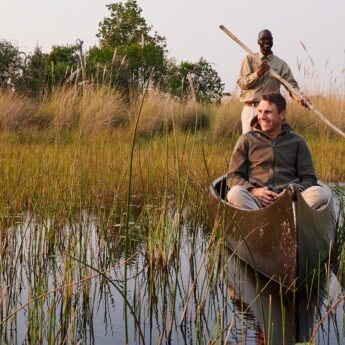 A guide steers a Mokoro through the river as a guide sits in the front, Sediba Sa Rona, Moremi Game Reserve, Botswana - Yellow Zebra Safari